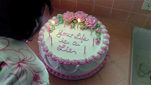 Gif of a pink and white cake that says "your life is a lie" written in icing